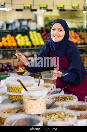 Jeune femme en hijab vendant des olives au supermarché Banque D'Images