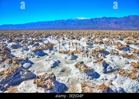 Devil's Golfcourse Salt formations avec des montagnes lointaines et des piscines d'eau sous la lumière du soleil Banque D'Images
