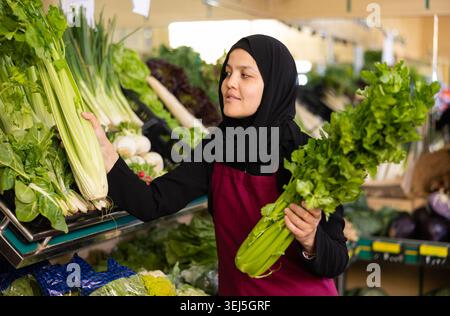 Jeune femme en hijab vend du céleri dans l'épicerie Banque D'Images