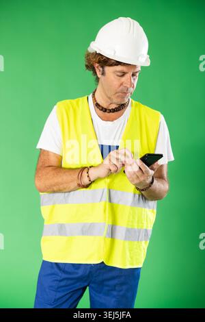 ingénieur portant un casque de sécurité tient un téléphone portable sur un fond vert Banque D'Images