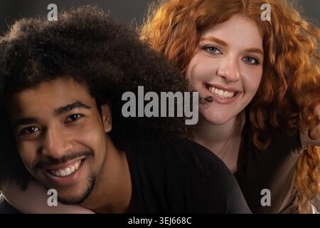 Heureux jeune couple diversifié embrassant, souriant et regardant la caméra Banque D'Images