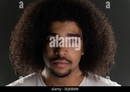 Jeune homme avec la coiffure afro et la pilosité faciale posant pour un portrait en gros plan Banque D'Images