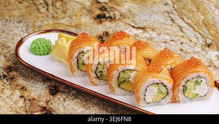 La nourriture, les rouleaux de Sushi remplis d'avocat et d'autres ingrédients sont soigneusement disposés sur une assiette. Le saumon orange vif domine les rouleaux, complété par du vert Banque D'Images