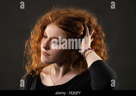 Femme rousse touchant ses cheveux bouclés, regardant vers le bas avec une expression réfléchie Banque D'Images