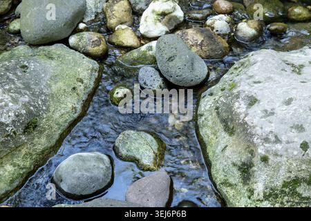 Un ruisseau peu profond coule sur des pierres lisses recouvertes de mousse dans la gorge de Pantalica, créant des reflets et de douces ondulations parmi les roches arrondies Banque D'Images