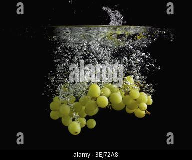 Raisins tombant dans l'eau avec des bulles d'air. Photo sur fond noir Banque D'Images