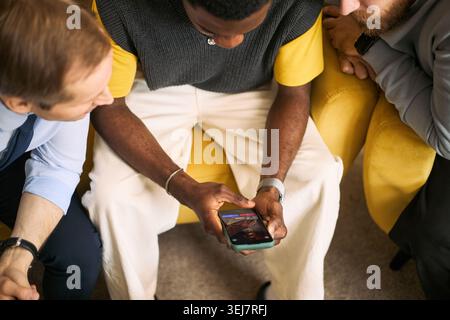 Vue en angle élevé de jeunes hommes adultes se rassemblant autour d'un smartphone, partageant du contenu et se liant par l'amitié masculine. Idéal pour la connexion sociale, la communauté, le marketing de style de vie Banque D'Images