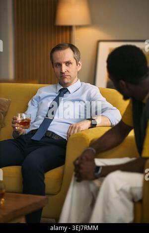 Plan vertical d'un homme caucasien d'âge moyen écoutant Black Friend au cours d'une conversation sérieuse, exprimant confiance et soutien. Idéal pour l'amitié, la santé mentale des hommes, les campagnes de conseil Banque D'Images