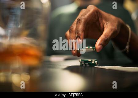 Gros plan de jeune homme noir empilant des jetons de poker pendant un match amical, suggérant des liens masculins et des loisirs. Convient pour les campagnes sur l'amitié, la vie nocturne, le risque Banque D'Images