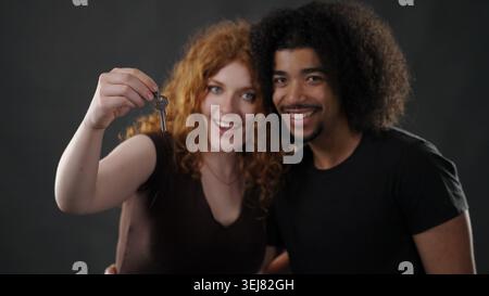 Heureux couple diversifié tenant les clés de la maison célébrant la propriété de la maison Banque D'Images