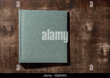 Couverture de livre en lin vert gris sur fond de bois foncé. Album photo en tissu fermé ou carnet sur une surface en bois rustique avec des ombres dures. Minimaliste Mo Banque D'Images