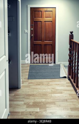 Couloir d'entrée de la maison avec porte en bois, tapis de sol et plancher de bois franc clair Banque D'Images