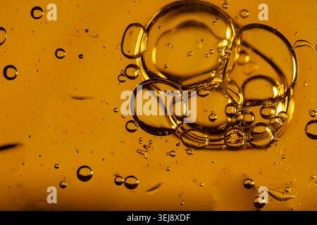Plan macro d'un liquide ambré texturé avec des gouttelettes d'huile flottantes et des motifs d'encre foncée tourbillonnants Banque D'Images