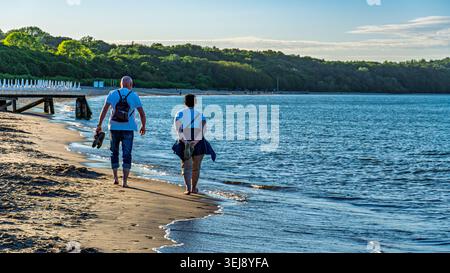 Couple senior marchant le long de la plage de sable par une journée ensoleillée au bord de la mer Baltique Banque D'Images