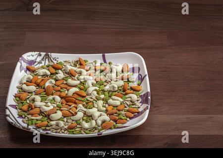 Gros plan de la variété de noix dans une plaque sur fond de table en bois. Graines de citrouille, graines de tournesol, noix de cajou et amandes. Protéines et graisses pour ve Banque D'Images