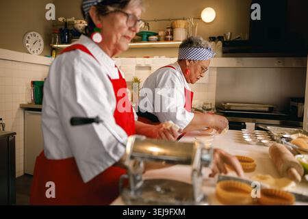Chefs femmes caucasiennes et noires actives préparant des pâtisseries dans un cadre de cuisine professionnel. Banque D'Images