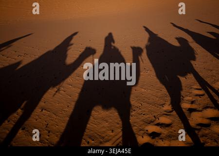 Ombres de voyageurs marchant à travers les dunes de sable du Sahara au Maroc, Afrique du Nord. Banque D'Images