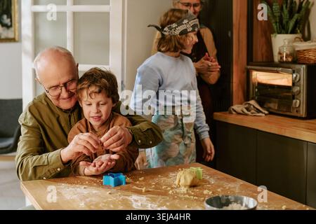 Homme senior aidant l'enfant à cuire des cookies dans la cuisine familiale Banque D'Images