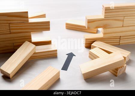 Mur en bois effondré fait de blocs et flèche de papier sur la table, gros plan. Surmonter les obstacles Banque D'Images
