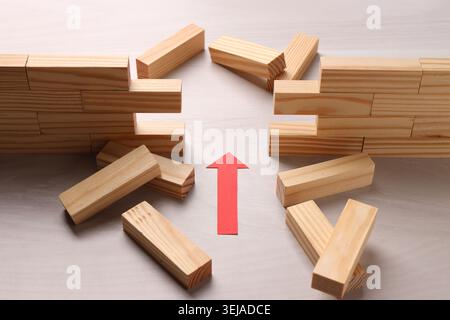 Mur en bois effondré fait de blocs et flèche de papier sur la table, gros plan. Surmonter les obstacles Banque D'Images