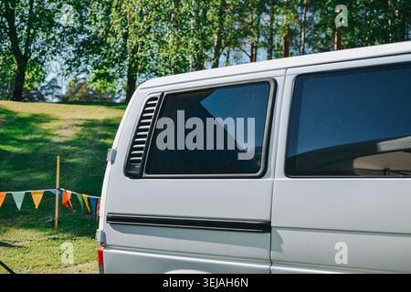 Riga, Lettonie - 23 mai 2026 : camping-car blanc moderne garé sur l'herbe verte dans un cadre de parc ensoleillé avec des arbres et des drapeaux colorés. Idéal pour voyager, CA Banque D'Images