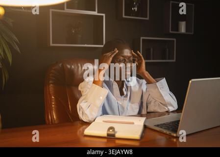 Jeune femme d'affaires ayant un mauvais mal de tête tout en travaillant sur un ordinateur portable tard dans la nuit, touchant les tempes, souffrant de la migration à cause du stress et plus Banque D'Images
