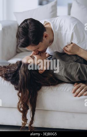 Un homme embrasse doucement son partenaire, capturant un moment tendre et affectueux entre eux alors qu'ils se détendent sur un canapé. Leur proximité dépeint un lien profond et Banque D'Images