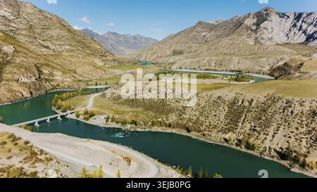 Serpentant à travers une vallée de montagne pittoresque, la rivière katun coule gracieusement, créant une boucle étonnante. Un pont et une route améliorent l'autum vibrant Banque D'Images