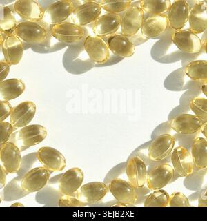 Capsules d'huile de poisson oméga-3 dorées disposées dans un motif circulaire sur fond blanc Banque D'Images