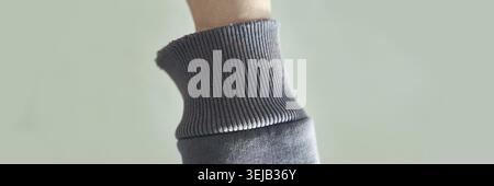 Gros plan confortable de tissu tricoté gris doux sur bras relevé sur fond vert Banque D'Images