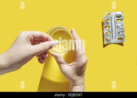Mains adultes caucasiennes tenant la pilule et le verre sur fond jaune vif avec blister vide Banque D'Images