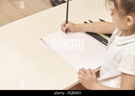 Femme asiatique dessinant portrait à table avec crayon et cahier dans une pièce lumineuse Banque D'Images