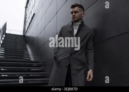 Élégant homme d'âge moyen caucasien en manteau appuyé contre le mur à l'extérieur Banque D'Images