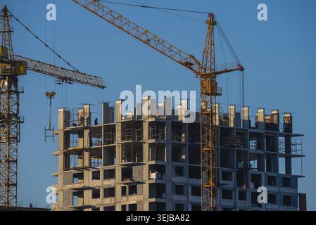 Grues de construction opérant sur un nouvel immeuble résidentiel sous un ciel bleu clair, mettant en évidence le développement urbain, la croissance et l'archi moderne Banque D'Images