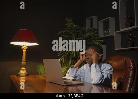 Jeune femme d'affaires afro-américaine massant ses temples, se sentant épuisée et souffrant d'un mal de tête après une longue nuit de travail sur le compu Banque D'Images