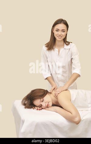 Thérapeute féminine donnant massage relaxant à une jeune femme caucasienne dans un cadre de spa avec atmosphère calme Banque D'Images