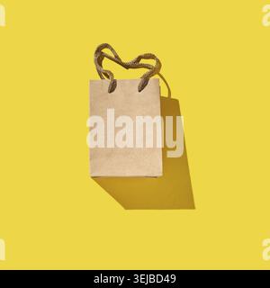 Sac en papier brun minimaliste avec poignée sur fond jaune vif jetant l'ombre Banque D'Images