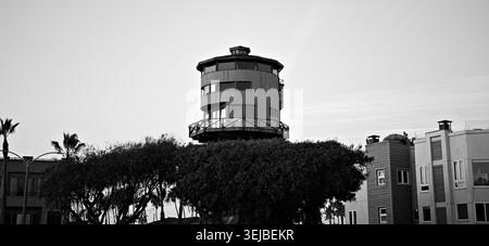 Tour de guet en bois s'élevant au-dessus des arbres au crépuscule à Sunset Beach, en Californie, encadrée par un ciel pastel doux et un quartier côtier calme. Banque D'Images