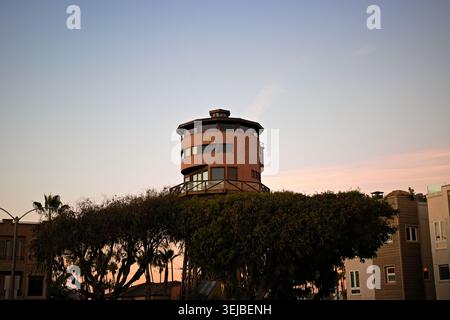 Tour de guet en bois s'élevant au-dessus des arbres au crépuscule à Sunset Beach, en Californie, encadrée par un ciel pastel doux et un quartier côtier calme. Banque D'Images