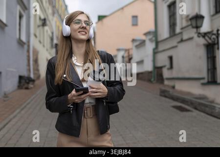 Jeune femme touriste dans des écouteurs avec un téléphone portable marche à travers la vieille ville Banque D'Images