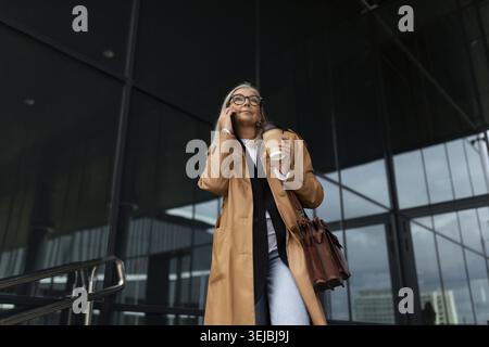 Femme âgée femme d'affaires quittant le bureau parlant sur un téléphone portable Banque D'Images