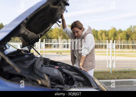 Conducteur féminin à côté du capot ouvert d'une voiture en panne Banque D'Images