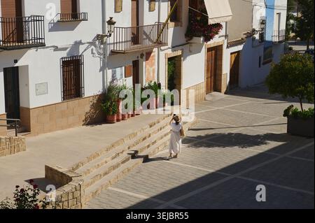 Une femme se promène dans un petit village espagnol ensoleillé, passant des maisons blanchies à la chaux, des pots en terre cuite et des marches en pierre tout en profitant de l'atmosphère médiévale Banque D'Images