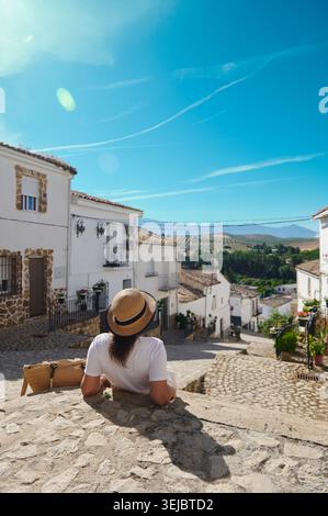 Femme voyageant à travers un petit village espagnol avec des maisons blanchies à la chaux et des rues pavées, assise dans un chapeau de paille et profitant de montages panoramiques Banque D'Images