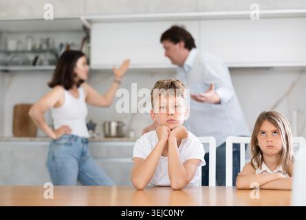 Frère et sœur assis à table pendant la querelle entre les parents Banque D'Images