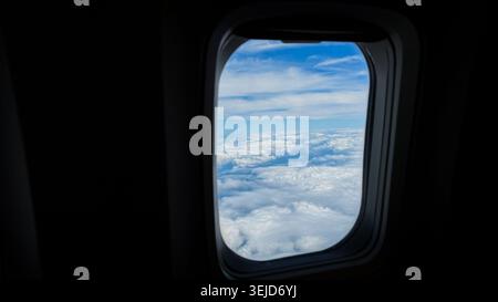 Vue de la fenêtre de l'avion montrant des nuages blancs pelucheux et un ciel bleu, avec un horizon clair visible au-delà du cadre de l'avion Banque D'Images
