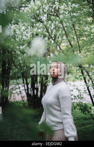 Jeune femme musulmane en hijab parmi les branches en fleurs dans Spring Park Banque D'Images