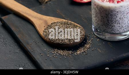 Graines de chia dans une cuillère en bois sur une table noire Banque D'Images