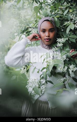 Élégante femme musulmane en hijab posant parmi les branches florissantes de printemps Banque D'Images