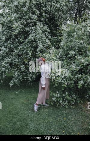 Femme musulmane debout sous l'arbre de printemps fleuri dans le jardin vert Banque D'Images